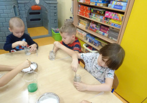 Trójka dzieci rozpuszcza sól w słoiczkach po przez mieszanie łyżeczką.